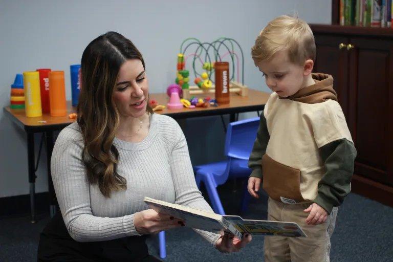 A BCBA-level therapist works with a toddler using a preferred activity — a picture book — as both an instructional medium and a rapport-building tool. Assent-based sessions begin with preference-based activities that establish trust before structured work is introduced.