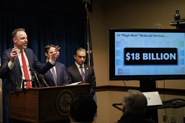 Acting U.S. Attorney Joseph Thompson at the December 18, 2025 Minneapolis press conference announcing EIDBI and Housing Stabilization Services fraud charges. The slide on the monitor behind him identifies $18 billion billed through 14 high-risk Medicaid programs since 2018 — the figure Thompson said had been at least half consumed by fraud.