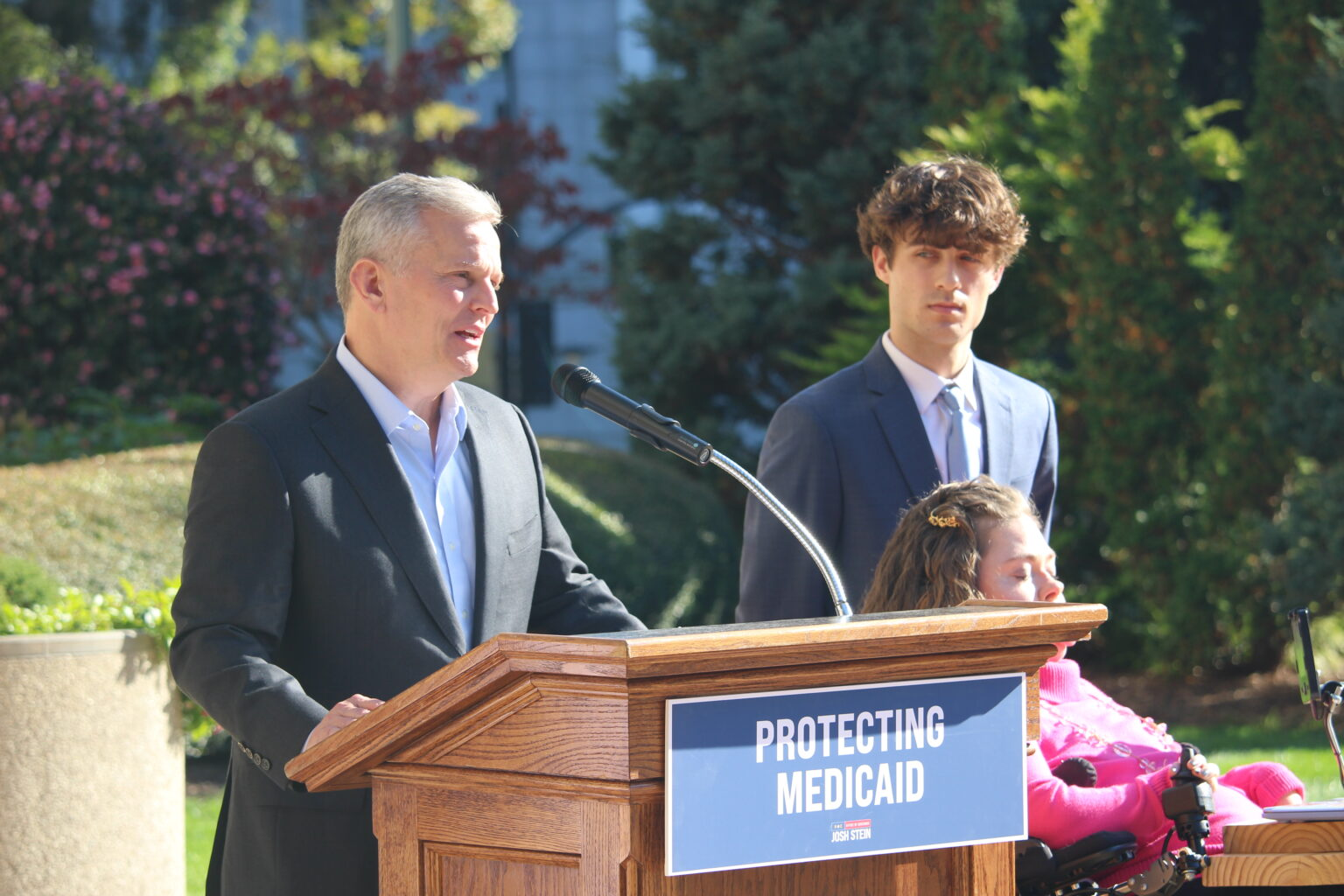 Governor Josh Stein speaks at an outdoor Medicaid press event during the budget standoff. Stein repeatedly framed the rate cuts as the legislature's failure, calling on Republican leadership to fully fund the program. The 