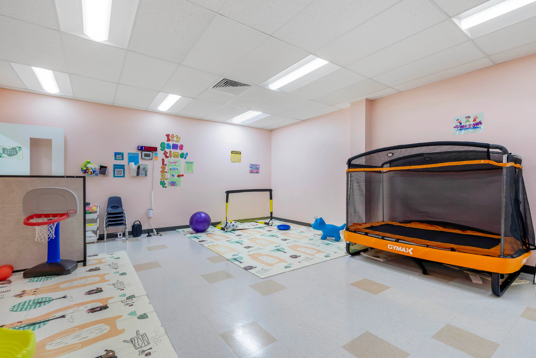 An ABA therapy gym equipped with a trampoline, basketball hoop, play mats, and sensory toys for structured and naturalistic play-based sessions.